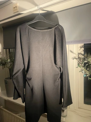 Svart långärmad kortklänning - Snygg svart kortklänning med lång ärm och djup urringning i ryggen. Klänningen har en enkel, stilren design och är tillverkad i ett mjukt material som sitter snyggt på kroppen. Perfekt för dig som gillar minimalistisk stil.