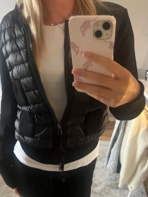  Moncler - Snygg svart pufferjacka från Moncler med quiltad framsida och dragkedja. Jackan har en klassisk passform och är perfekt för kyligare dagar. Ikonisk Moncler-logga på ärmen och stilren design som funkar till det mesta.