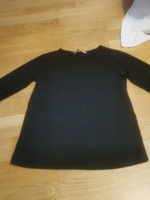 Svart långärmad tröja - En enkel svart långärmad tröja med rund hals. Tröjan har en rak passform och är tillverkad i ett mjukt material som passar perfekt till olika outfits. Stilren och lätt att matcha med andra plagg.