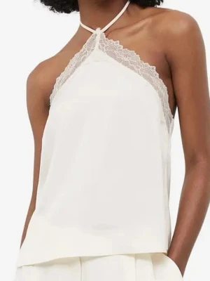 Vit top med spets  - Säljer en stilren vit halterneck topp med tunna axelband och fina spetsdetaljer längs ringningen. Toppen har en lös passform och är tillverkad i ett glansigt, mjukt material som ger en lyxig känsla.