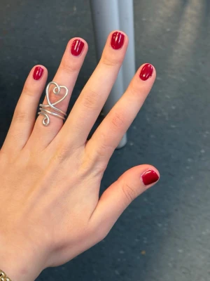 Silvrig ring med hjärtformad design - Unik silvrig ring i metall med en öppen, virad design som formar ett hjärta på ovansidan. Ringen har en modern och lekfull look med flera slingrande band runt fingret. Perfekt för dig som vill ha ett statement-smycke med romantisk touch.