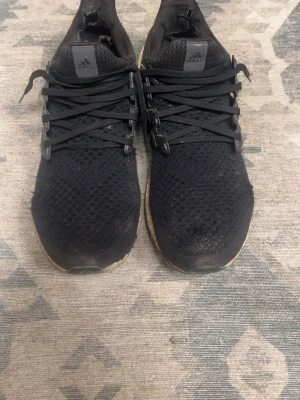 Svarta Adidas Ultra Boost sneakers - Svarta Adidas Ultra Boost sneakers med stickad ovandel och klassiska tre ränder på sidan. Skorna har svart snörning och en vit, dämpad sula i Boost-material. Perfekta för dig som gillar sportig och stilren look. Väldigt unika och svåra att få tag på. Priset kan diskuteras vid snabb affär.