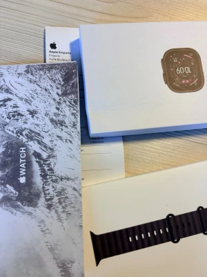 Apple Watch Ultra 3 - Säljer en Apple Watch med svart sportarmband. Klockan har en fyrkantig skärm och levereras i originalförpackning med tillhörande manual. Perfekt för dig som vill ha koll på notiser, träning och hälsa direkt på handleden.
