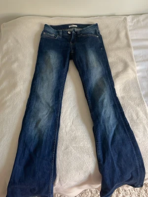 Blå bootcut jeans med kvarg färg från Gina - Säljer ett par blå bootcut jeans med snygg kvarg färg. Jeansen har klassisk femficksdesign och ganska låg midja. Perfekta för en avslappnad och trendig look. Nypris 500kr och jag säljer för 150kr.