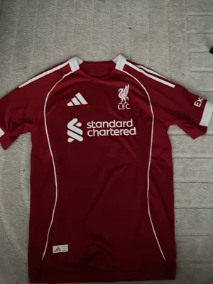 Liverpool matchtröja Virgil #4 Adidas - Röd Liverpool matchtröja från Adidas med vita detaljer och tryck. Framsidan har klubbmärke och sponsorlogga, baksidan har namnet 'Virgil' och nummer 4. Tillverkad i funktionsmaterial, perfekt för fotboll eller träning.