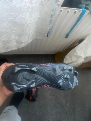 Nike rosa/svarta fotbollsskor - Säljer ett par puma fotbollsskor med svart och rosa mönster samt svarta skosnören. Skorna har en slitstark sula med dobbar för bra grepp på planen och är tillverkade i syntetmaterial. Perfekta för dig som vill sticka ut på fotbollsplanen.