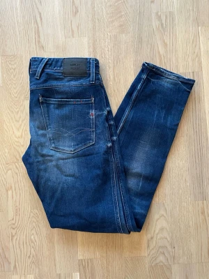 Mörkblå Replay Anbass jeans W32 L34 - Jag säljer dom här fina Replay Anbass jeansen i storlek W32 L34. De är i fint skick med snygga slitningar. Tveka inte att höra av er!                     Mått: Längd=107cm. Midja=44cm