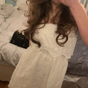 Vit axelbandslös klänning med spets - Söt vit axelbandslös klänning med broderade spetsdetaljer och volang upptill. Klänningen har en kort längd och ett luftigt, somrigt material som känns lätt att bära. Perfekt för sommaren! Inga defekter utan i helt felfritt skick!💕