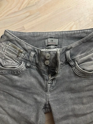 Lågmkdjade jeans LTB  - Snygga grå jeans från LTB med två knappar i midjan och dragkedjedetalj på fickan. Klassisk femficksmodell med smal passform och bootcut. Perfekta för en trendig och avslappnad stil. Lågmidjade! 