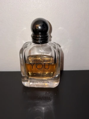 Emporio Armani Stronger With You parfym - Emporio Armani Stronger With You parfym i en stilren, transparent glasflaska med rundad svart kork. Doften har en varm bärnstensfärgad vätska och flaskan har eleganta linjer och tydlig logga framtill.