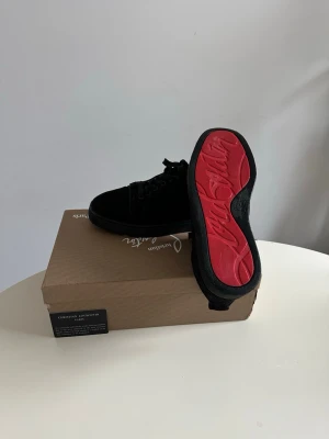 Svarta sneakers från Christian Louboutin - Snygga svarta sneakers från Christian Louboutin i mocka med klassisk röd sula och diskret logga undertill. Lågt skaft och svarta skosnören ger en clean look. Perfekta för dig som vill ha något exklusivt och stilrent. Kan också byta /helst valentinos 