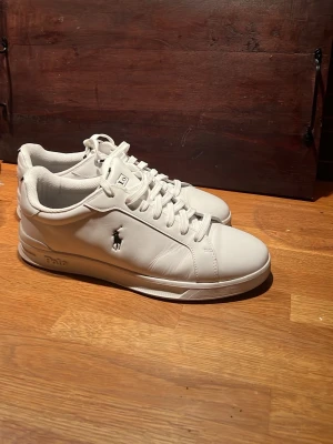 Vita sneakers från Polo Ralph Lauren - Säljer ett par fräscha vita sneakers från Polo Ralph Lauren med klassisk logga på sidan. Skorna har snörning, rund tå och är gjorda i syntetläder med insida i polyester och yttersula i gummi. Perfekta till jeans eller shorts för en clean look. Köpta på Zalando men låda och kvitto följer inte med, men tveka inte vid fler frågor🙌