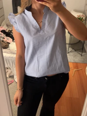 Blårandig blus med volangärm - Snygg blus med tunna blå och vita ränder, korta volangärmar och v-ringad hals. Lätt och luftig modell som ger en fräsch look. Perfekt till jeans eller kjol. Materialet känns mjukt och bekvämt mot huden.