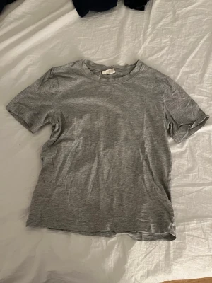 Grå basic t-shirt i bomull - En enkel grå t-shirt i mjuk bomull med rund hals och korta ärmar. Modellen är klassisk och passar perfekt till jeans eller shorts. T-shirten har en normal passform och är ett måste i garderoben för en clean och avslappnad stil.