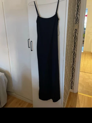 Svart långklänning Gina Tricot - Säljer en svart långklänning från Gina Tricot med smala axelband och rak passform. Klänningen är enkel och stilren, perfekt för dig som gillar minimalistisk stil. Materialet känns mjukt och följsamt mot kroppen.