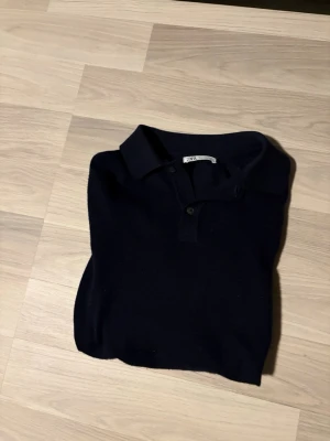 Svart pikétröja från Zara - Klassisk svart/mörkblå pikétröja från Zara med krage och två knappar framtill. Tröjan har en stilren look och är tillverkad i mjukt material som passar perfekt till olika outfits. Enkel att matcha och ett måste i garderoben. Hör av er vid minsta fundering!