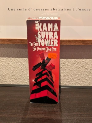 Kama Sutra Tower spel - Roligt sällskapsspel med temat Kama Sutra Tower. Spelet kommer i en röd och svart kartong med vita illustrationer och text. Perfekt för att liva upp kvällen med vänner eller partner. Innehåller spelbitar och instruktioner på engelska.