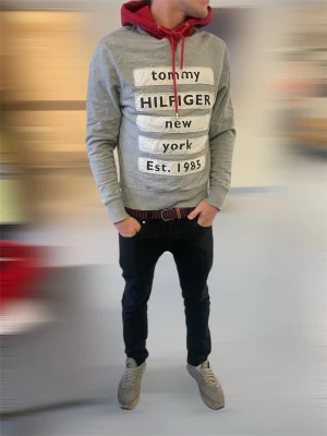 Grå och röd hoodie Tommy Hilfiger M - Snygg grå hoodie från Tommy Hilfiger med röd huva och snörning. Framsidan har stora vita tryck med texten 'tommy HILFIGER new york Est. 1985'