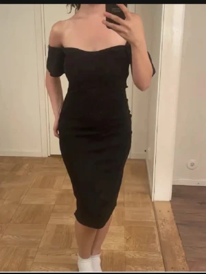 Svart offshoulder klänning - Säljer en svart, figurnära klänning med offshoulder-design och medellång längd. Klänningen har en enkel och stilren look, perfekt för dig som gillar minimalistisk stil. Materialet känns mjukt och följsamt mot kroppen.