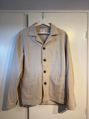 Beige overshirt från John Henric - Stilren beige overshirt från John Henric i ett lätt, luftigt bomullstyg. Perfekt till sommaren! Skick: 9,5/10 oanvänd. Pris 399. Storlek: s. Bara att fråga om det är något!