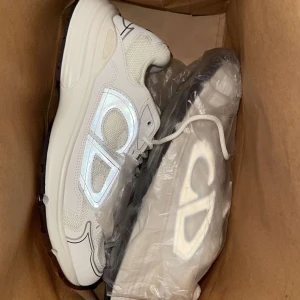 Dior b20 - Säljer ett par vita New Balance 530 sneakers med reflekterande detaljer och meshpaneler för extra ventilation. Skorna har en chunky sula och klassisk logga på sidan. Perfekta för dig som gillar sportig och clean stil.