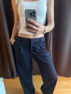 Mörkblå kostymbyxor med pressveck - Säljer ett par mörkblå kostymbyxor med raka ben och pressveck framtill. Byxorna har hög medel/låg midja. Oanvända. 