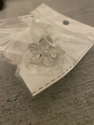 Silverfärgad blomring i metall - Säljer en helt ny silver ring i form av en blomma. JUSTERINGSBAR. Minns dock inte vart jag köpte den.
