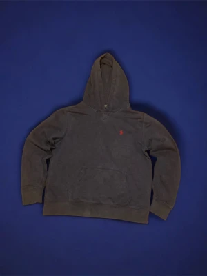 Mörkblå hoodie från Polo Ralph Lauren - Mörkblå hoodie från Polo Ralph Lauren med klassisk röd broderad logga på bröstet. Hoodien har en stor huva och magficka framtill. Tillverkad i mjukt bomullsmaterial som känns skönt mot huden. Perfekt för en avslappnad och stilren look.