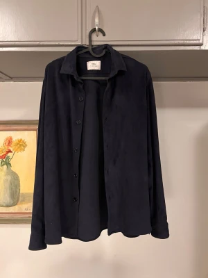 Mörkblå skjorta från Ciszere - Stilren mörkblå skjorta från Ciszere i mjukt material med klassisk krage och knappar framtill. Skjortan har lång ärm och en avslappnad passform som passar perfekt till olika outfits. Enkel och tidlös design utan mönster eller extra detaljer.