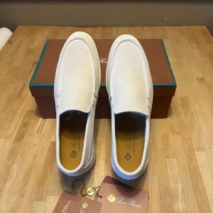 Vita loafers från Loro Piana - Snygga vita loafers från Loro Piana i textilmaterial med klassisk siluett och diskreta sömmar. Skorna har en stilren design med låg sula och är perfekta för en clean och avslappnad look. Märkets logga syns på innersulan.