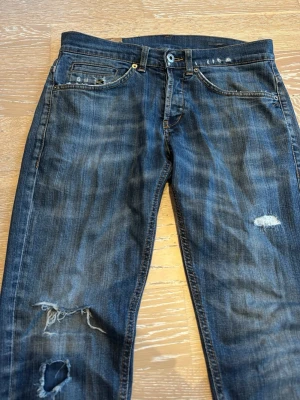 Blå slitna jeans med hål - Säljer ett par blå jeans med slitningar och slitningar på benen (original från butik) Klassisk femficksmodell med knappgylf och smal passform. Mycket populära och eftertraktade. Mycket bra skick (lappen inuti är sönder). 