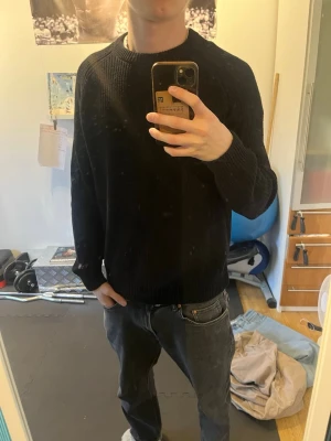 Svart stickad tröja med rund hals - En enkel och stilren svart stickad tröja med rund hals och långa ärmar. Tröjan har ribbstickade muddar vid ärmslut och nederkant. Perfekt för lager-på-lager och passar till jeans eller chinos. Materialet är mjukt och bekvämt.