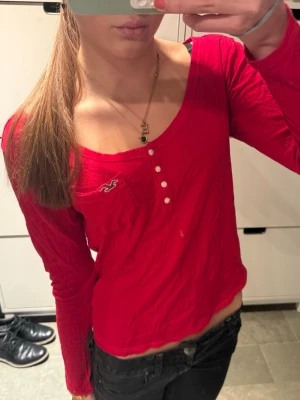 Hollister henley röd långärmad topp - Snygg röd långärmad topp från Hollister med knappar framtill och liten logga på bröstet.                   Storlek M men passar S bättre!