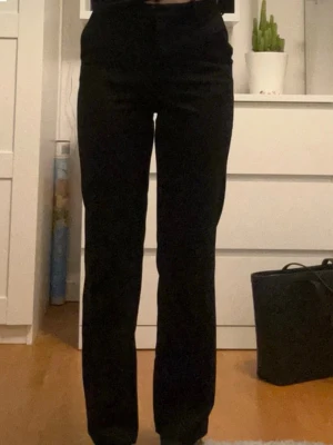 Svarta raka kostymbyxor - Snygga svarta kostymbyxor med rak passform och klassisk midja. Perfekta för en stilren look och lätta att matcha med olika toppar. Byxorna har diskreta fickor och stängs med dragkedja och knapp framtill.
