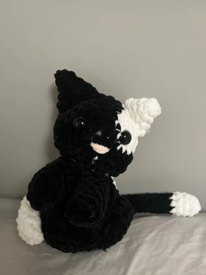 Virkad svartvit kattmjukis - Supergullig handvirkad katt i svart och vitt garn med stora svarta ögon och rosa nos. Katten har en lång svans, ett svart och ett vitt öra samt vita detaljer på tassar och svans. Perfekt som dekoration eller mysig kompis.