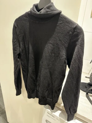 Svart polotröja från J.Lindeberg - Snygg svart stickad polotröja från J.Lindeberg. Tröjan har lång ärm, ribbade muddar och hög polokrage. Är i storlek L men passar också M. Perfekt för lager-på-lager och enkel att matcha med andra plagg. Klassisk och stilren design som funkar året runt. Skriv över det minsta lilla eller över den minsta funderingen!🔥🔥