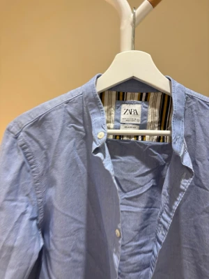 Blå henley-skjorta från Zara - Ljusblå henley-skjorta från Zara med lång ärm och knappar upptill. Skjortan har en avslappnad passform och är tillverkad i mjuk bomull. 