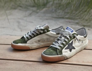 Golden Goose sneakers med grön mocka - Snygga Golden Goose sneakers i vitt skinn med gröna mockadetaljer och svart stjärna på sidan. Skorna har grå snörning, orange gummisula och GGDB/SSTAR-tryck i guld. Klassisk streetstil med slitna detaljer och låg profil. Obs: lnte 0rglnal‼️Men skorna otroligt snygga och gjorda i mycket kvalitet. Skostorlek 44 med innersulans mått på ca 28 cm. HELT NYA