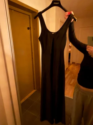 Svart långklänning från Weekday - En stilren svart långklänning från bikbok med ärmlös design och rundad halsringning. Klänningen har en rak och enkel siluett i ett mjukt, glansigt material som ger en snygg look. Perfekt för dig som gillar minimalistisk stil.