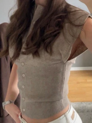 Beige kortärmad stickad kofta - Superfin beige stickad kofta med korta ärmar och knappar framtill. Modellen är croppad och sitter tajt. Mjuk och skön kvalitet, enkel att matcha till olika outfits. Använd ett fåtal gånger. 