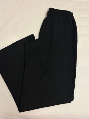 Svarta loungewear-byxor med dragsko från Gina Tricot  - Ett par svarta mjukisbyxor med bred och avslappnad passform från Gina Tricot i storlek XXS. Byxorna har resår i midjan samt dragsko för justerbar komfort. Tillverkade i ett mjukt, strukturerat tyg som känns skönt mot huden. 