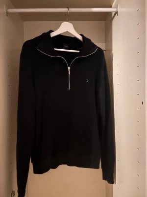 Svart halvzip tröja från Boomerang - Svart långärmad tröja från Boomerang med halvzip och liten broderad logga på bröstet. Tröjan har en hög krage och ribbade muddar vid ärmslut och nederkant. Perfekt för en avslappnad och stilren look.