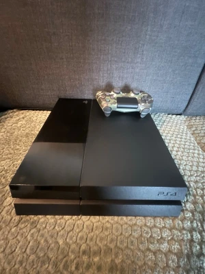 Sony PlayStation 4 med camo-handkontroll - Säljer en svart PlayStation 4 från Sony med en DualShock 4-handkontroll i camouflage-mönster. Konsolen har en stilren, rektangulär design i plast och mattsvart finish. Perfekt för gaming och streaming av film och serier. Kontrollen är som ny köpte den för drygt 2 månaders 
