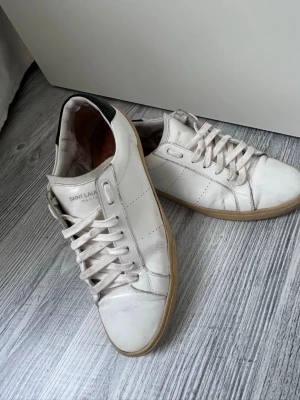 Vita Saint Laurent sneakers i läder - Äkta saint Laurent skin skor vita, har Tycärr inte orginal sulan eftersom dem gick i sönder och lådan har jag inte iheller. Men dem ska va äkta eftersom dem olika koderna, nummererna, bokstäverna och skinet. Men skicka gärna om ni har några frågor, funderingar eller vill ha några fler bilder. Skulle säga att skorna är mellan mycket bra och bra skick 