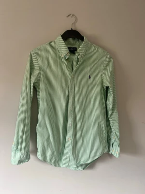 Grön- och vitrandig skjorta Ralph Lauren - Snygg grön- och vitrandig skjorta från Ralph Lauren med klassisk krage och knappar framtill. Skjortan har lång ärm och den ikoniska broderade loggan på bröstet. Tillverkad i mjuk bomull som känns skön mot huden. Pris går att diskuteras vid snabb affär!!
