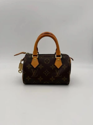 Louis Vuitton Min Speedy väska - Tidlös investering. Begagnad lyxväska LOUIS VUITTON NANO SPEEDY med monogram. Mångsidig och slitstark väska som erbjuder ikonisk stil och premiumkvalitet.