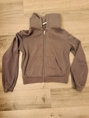 Brun zip hoodie från 157 XS - Mysig brun hoodie från 157 i storlek XS. Tröjan har dragkedja framtill, två fickor och en stor huva. Tillverkad i mjukt material med ribbade muddar vid ärmar och nederkant. 