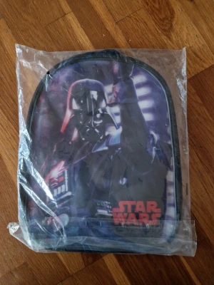 Star Wars ryggsäck med Darth Vader - Cool ryggsäck med Darth Vader-motiv från Star Wars. Svart basfärg med färgstarkt tryck på framsidan och justerbara axelband. Perfekt för dig som gillar Star Wars och vill ha en unik väska till skolan eller utflykten.