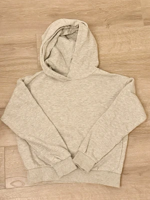 Ljusgrå basic hoodie Kappahl 146/152 - En enkel och stilren ljusgrå hoodie med huva. Tillverkad i mjukt sweatshirtmaterial och har ribbade muddar vid ärmslut och nederkant. Perfekt för en avslappnad och bekväm look. Storlek 146/152