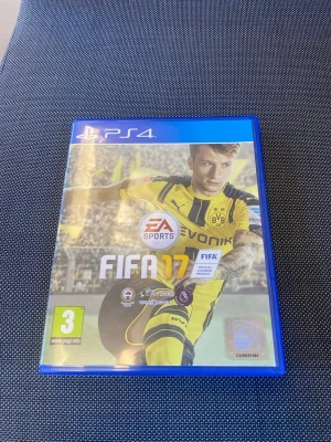 FIFA 17 till PS4 - FIFA 17 till PlayStation 4 med blå plastfodral. Omslaget visar en fotbollsspelare i gul och svart matchtröja från Borussia Dortmund. Spelet är ett fotbollsspel och innehåller FIFA Ultimate Team-läge. Skivan och fodralet är med på bilden.